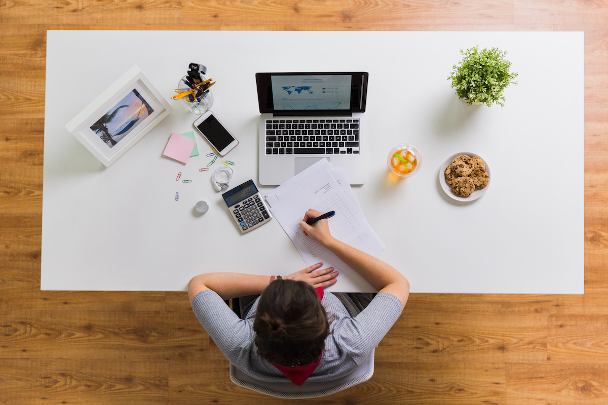 Frau erstellt Businessplan mit Taschenrechner und Unterlagen am Bürotisch